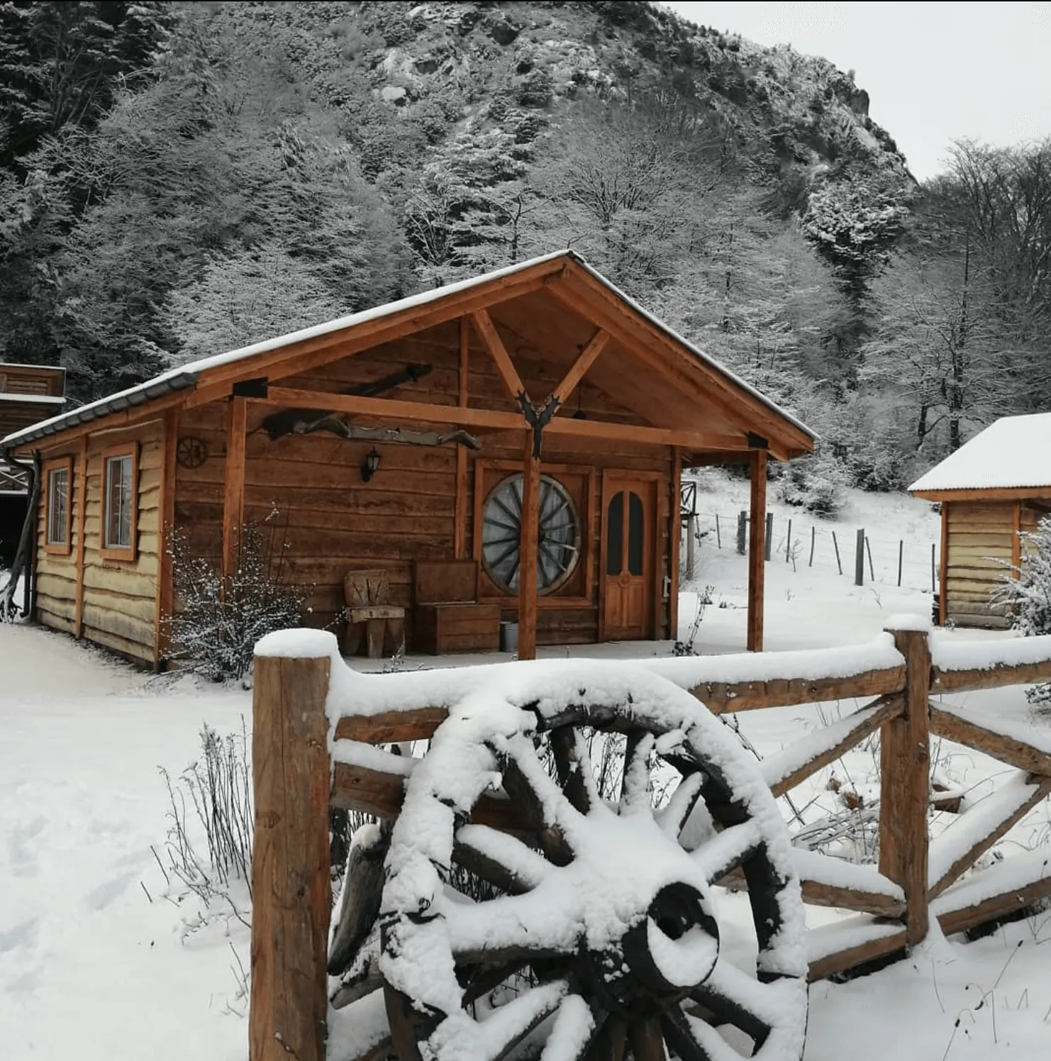 Una cabaña en invierno, con la rueda de carreta nevada en el cerco
